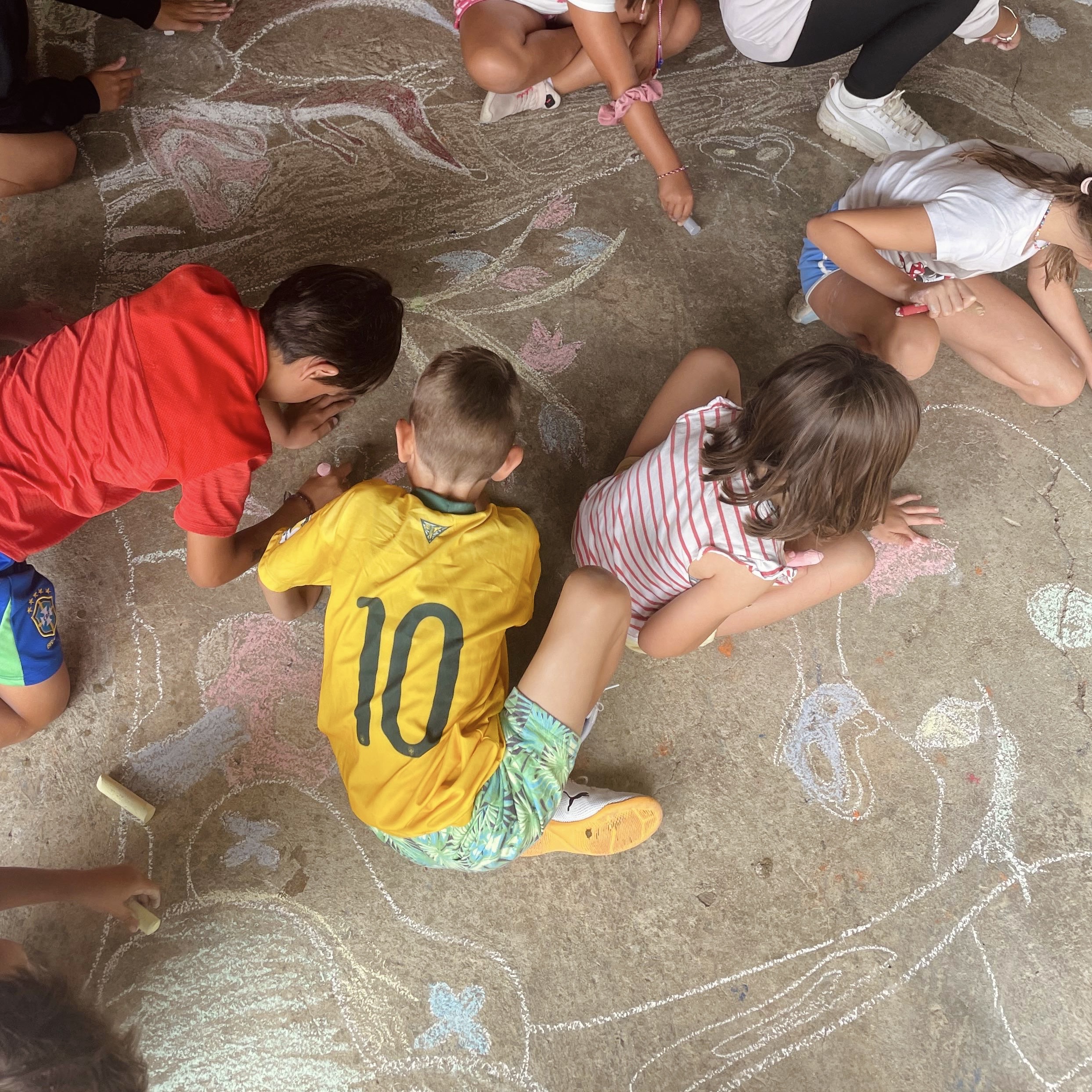 actividad-artistica-infantil-extraescolares-granja-naturalia-esquiroz Niños dibujando con tizas de colores en el suelo durante una actividad artística en la granja escuela Naturalia de Esquíroz