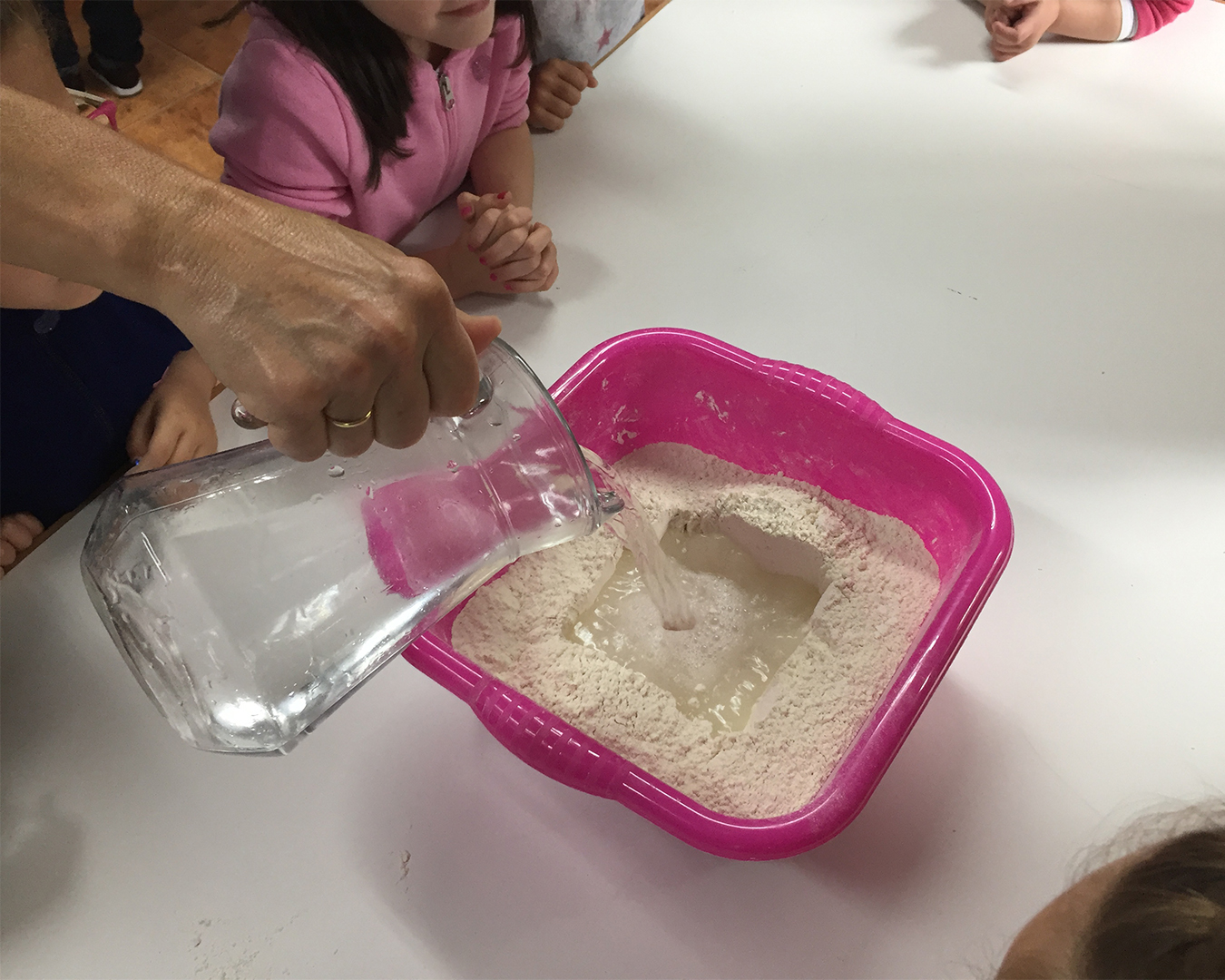 ninos-aprendiendo-hacer-pan-granja-naturalia-esquiroz-taller Niños añadiendo agua a la harina en una actividad práctica de pan casero en la granja escuela Naturalia de Esquíroz